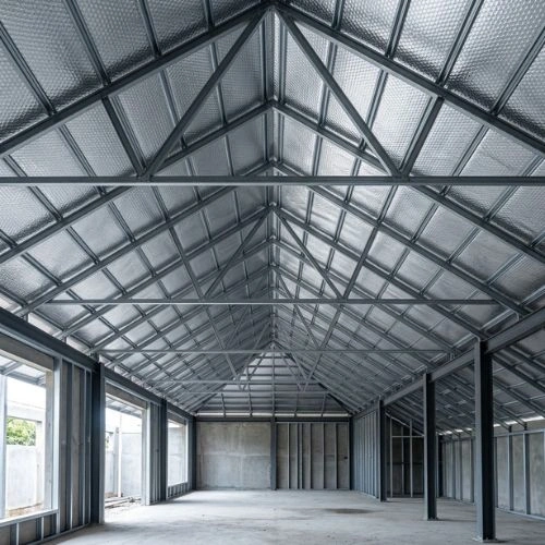 Interior of an unfinished industrial warehouse with exposed steel framing, concrete floor, and large window openings along the left wall.